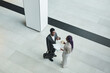 © Seventyfour - Top down view at two African-American business people chatting in office hall against graphic floor background, copy space