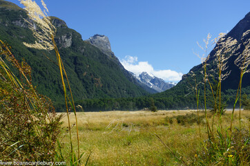 Canvas Print - Grassy river flat between converging mountains