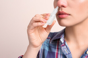 Canvas Print - Woman using nasal spray on beige background, closeup. Space for text