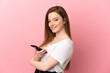 © luismolinero - Teenager girl over isolated pink background holding a mobile phone and with arms crossed