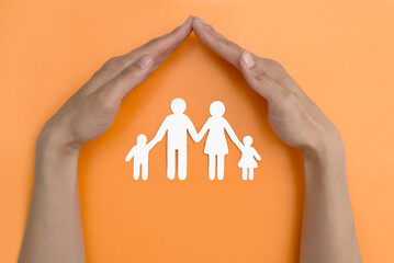 the concept of social protection of families with children. social assistance, family support. hands hold a paper figure of a family on an orange background