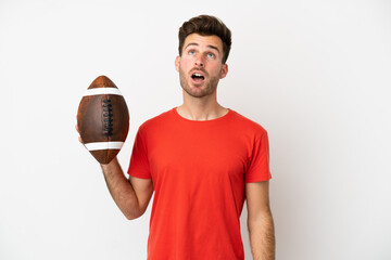 Young caucasian man playing rugby isolated on white background looking up and with surprised expression