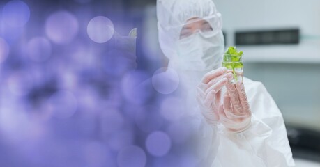 Poster - Female scientist in ppe suit holding beaker with plant in laboratory with purple spots