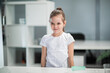 Portrait of a little girl in a white T-shirt on the background of a shelf, the girl wrinkles her nose, she is dissatisfied
