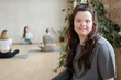 © pressmaster - Brunette female with Down syndrome looking at you while group of girls practicing yoga in gym