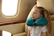 © New Africa - Cute little girl with travel pillow sitting in airplane during flight