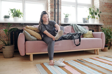 Wall Mural - Disable girl with Down syndrome putting sports-shoes on while sitting on couch in living-room