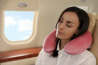 © New Africa - Young woman with travel pillow sleeping in airplane during flight