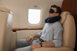 © New Africa - Young man with travel pillow and mask sleeping in airplane during flight
