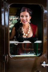 Wall Mural - Beautiful female in vintage red dress looking at camera through train door window