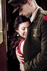 Wall Mural - Vintage couple, man in uniform, holds woman in red dress close to his chest with train in background