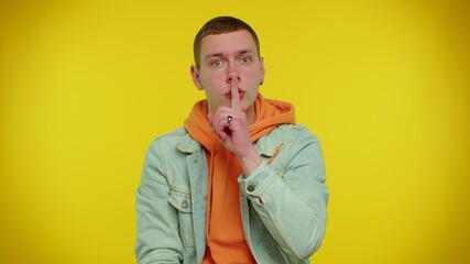 Keep my secret. Do not tell anyone. Shh be quiet please. Teenager student boy 20s years old presses index finger to lips makes silence gesture sign. Young adult man posing on yellow studio background