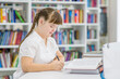 © Ermolaev Alexandr - Clever young girl with down syndrome doing homework at library. Education for disabled children concept
