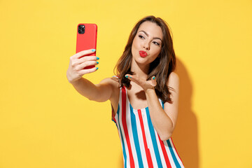 Happy young sexy woman slim body wear striped red blue swimsuit doing selfie hold mobile cell phone isolated on vivid yellow color wall background studio Summer hotel pool sea rest sun tan concept