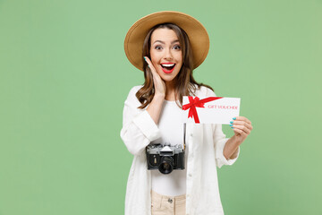 Traveler shock tourist woman in casual clothes hat camera hold gift voucher flyer mock up hold face isolated on green background Passenger travel abroad on weekends getaway Air flight journey concept.