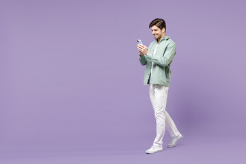 Wall Mural - Full length young fun happy man in casual mint shirt white t-shirt using mobile cell phone chat online in social network walk isolated on purple background studio portrait People lifestyle concept.