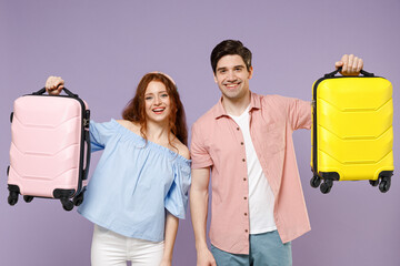 Two smiling happy traveler tourist woman man couple in shirt hold yellow pink suitcase valise bag isolated on purple background. Passenger travel abroad weekends getaway. Air flight journey concept