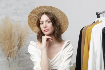 Wall Mural - Portrait of young fashionable woman sitting next to clothing rack in fashion atelier or personal wardrobe.	