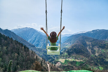 Wall Mural - Free happy joyful woman traveler with open arms swinging on chain swing in the mountains, enjoying beautiful view and good life moment