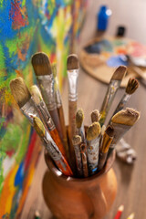 Poster - Paint brush in clay jug and palette on wooden table background. Oil painting and art still life