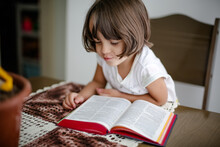 Criança Em Cima Da Mesa Lendo A Bíblia Sagrada E Folheando.