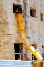 Suspended Sections Of Yellow Garbage Chute On A Facade Of Building Under Construction, Debris Chutes