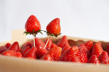 red strawberries in a wooden box and two strawberries on a toothpicks on a white background