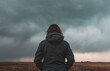 Woman standing in meadow, looking at the horizon and dark dramatic stormy clouds, rear view