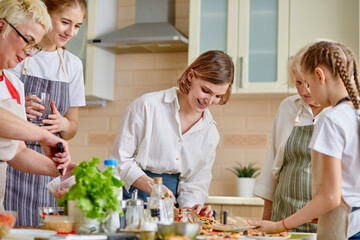 Wall Mural - Side view portrait of attractive ladies grandmoms and children cooking. making dough and ingredients for pizza and other meal, wearing apron. at home in kitchen