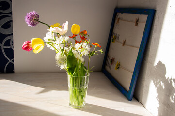 bouquet of colorful bright garden flowers in vase  on white table and blue love picture frame