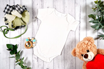 Baby wear romper onesie flatlay. On-trend farmhouse theme craft product mockup with farmhouse style decor, on a white wood background. Negative copy space for your design here.