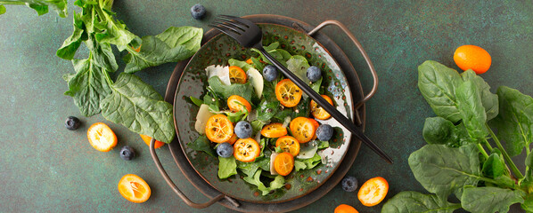 Wall Mural - bowl of salad with spinach, cheese, kumquat and blueberries on a dark table