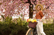 Beautiful young woman with bicycle and flowers in park on pleasant spring day. Space for text