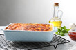 Tasty cooked lasagna in baking dish on white marble table