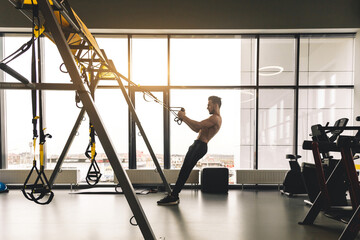 Handsome young sporty male bodybuilder with naked torso doing exercises in the gym