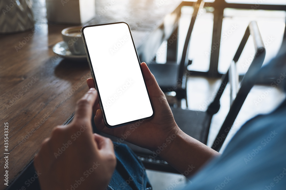 Mockup image of a woman holding and using mobile phone with blank white desktop screen with coffee cup on the table - obrazy, fototapety, plakaty 
