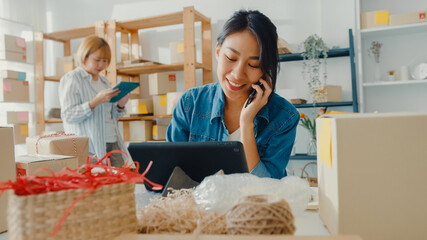 Young Asia businesswomen using mobile phone call receiving purchase order and check product on stock work at home office. Small business owner, online market delivery, lifestyle freelance concept.