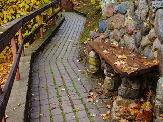 Wall Mural - Small stone path in a park and a bench made with stone covered with fallen leafs. Fall or autumn season concept