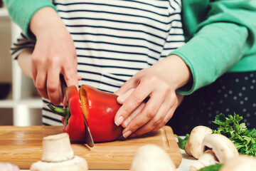 Mother teaches her daughter to cutting peper for salad, closeup. Mom and child cooking fresh salad together.