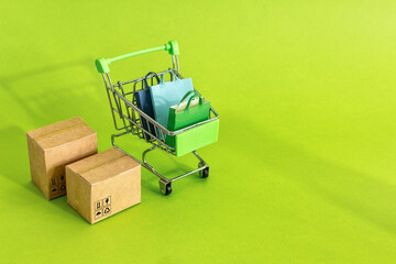 Canvas Print - Cardboard boxes or paper boxes in shopping cart on green background. Online shopping and delivery service concept.