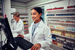 © StratfordProductions - Young female pharmacist using computer with senior colleague using digital tablet in chemist