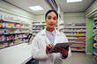 © StratfordProductions - Portrait of young african american female standing near counter in pharmacy using digital tablet