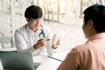 Wall Mural - Confident doctor man holding a pill bottle while talking with a senior patient and reviewing his medication at office room.