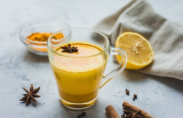 A beautiful glass with golden milk, turmeric, spices and lemon on a gray background. Healthy Ayurvedic drink. Strengthening the immune system. Antioxidant and superfood