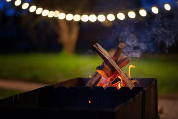 Wooden logs burning in the grill in the night garden decorated with lanterns. summer parties with grill cocept