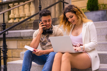 Young entrepreneurs doing teamwork. Working on the internet with the computer, boy with music headphones and girl in white suit