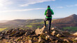 Hiker with a backpack on a rocky mountain peak looking in the distance. Landscape from Little Sugar Loaf peak in Wicklow Mountains, Ireland.