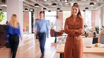 Wall Mural - Portrait Of Businesswoman By Desk In Busy Multi-Cultural Office With Motion Blurred Colleagues