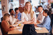 © Monkey Business - Portrait Of Businesswoman With Colleagues In Background Sitting Around Table In Open Plan Office