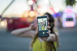 © MiguelAngelJunquera - Mujer joven atractiva en vestido de verano haciendo un selfie en el parque de atracciones visto a través de la cámara del smarpthone